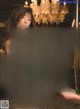 A naked asian woman sitting on a pole in front of a chandelier.