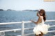 A woman in a white dress standing on a railing by the water.