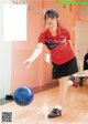 A woman in a red shirt and black skirt playing bowling.