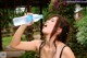 A woman drinking water from a bottle in a park.