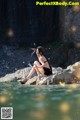 A woman sitting on a rock in the water.