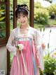 A woman in a pink and blue hanbok holding a flower.