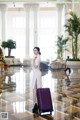 A woman in a white dress standing next to a purple suitcase.