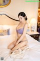 A woman in a purple lingerie sitting on a bed.