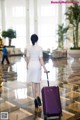 A woman in a white dress with a purple suitcase.