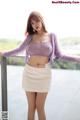 A woman in a purple sweater and white skirt posing for a picture.