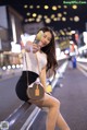 A woman sitting on a railing taking a selfie.