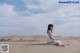 A woman in a white dress sitting on a sand dune.