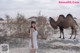 A woman in a white dress standing next to a camel.