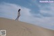 A woman in a white dress standing on top of a sand dune.