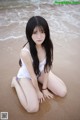 A woman in a white bathing suit sitting on the beach.