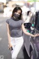 A woman wearing a face mask standing next to a car.