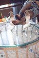 A woman sitting on top of a glass table next to a bowl of fruit.