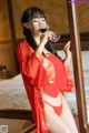 A woman in a red robe drinking a glass of wine.