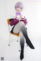 A woman sitting on a chair wearing a purple wig and black stockings.