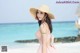 A woman in a pink dress and straw hat on the beach.