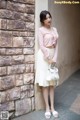 A woman leaning against a brick wall with a handbag.