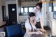 A woman sitting at a desk writing on a piece of paper next to another woman.