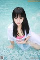 A woman in a white shirt and pink bikini sitting in a pool.