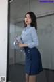 A woman in a blue shirt and skirt holding a clipboard.