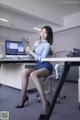 A woman sitting at a desk in an office holding a clipboard.