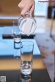 A person pouring water into a glass on a table.