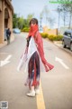 A woman wearing a red scarf standing on the side of a road.