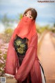 A woman wearing a red veil standing on a dirt road.