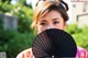 A woman holding a black fan in front of her face.