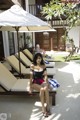 A woman in a bathing suit sitting on lounge chairs by a pool.