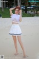 A woman in a white top and skirt standing on a beach.