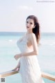 A woman in a white dress standing on a balcony overlooking the ocean.