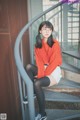 A woman sitting on a set of stairs wearing a red sweater and black tights.