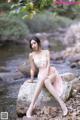 A woman sitting on a rock by a stream.