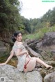 A woman sitting on a rock by a river.