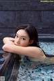 A woman in a swimming pool with her arms resting on the edge of the pool.