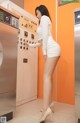 A woman in a white dress standing in front of a washing machine.