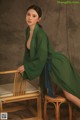 A woman in a green dress sitting on a wooden chair.