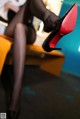 A woman sitting on top of a yellow chair wearing black stockings and red shoes.