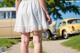 A woman in a white dress standing in front of a yellow car.